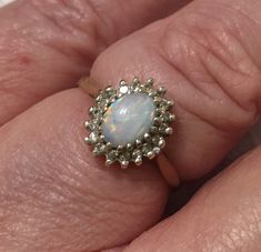 a woman's hand holding a ring with an opal in the center and diamond accents