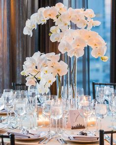 an elegant centerpiece with white orchids and candles sits atop a table set for dinner