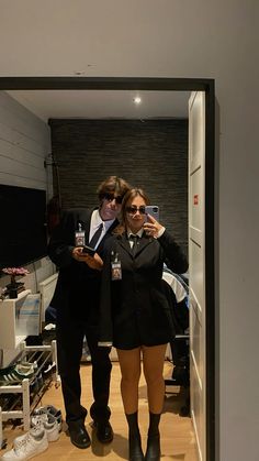 a man and woman standing in front of a mirror taking a selfie with their cell phones