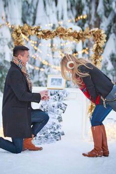 a man kneeling down next to a woman in the snow while she holds her purse