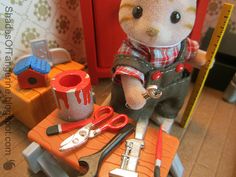 a toy cat sitting on top of a table next to scissors and other items in front of him