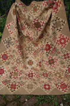 an old quilt is laying on the ground in front of some bushes and trees,