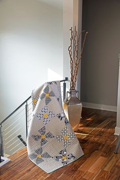 a vase with some flowers in it sitting on the floor next to a quilted blanket