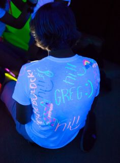 a young boy sitting on the ground in front of a neon shirt with writing on it