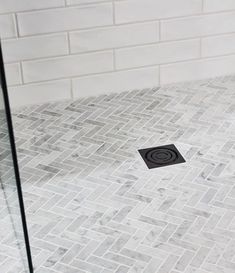 a white tiled bathroom with a black square in the floor and a shower stall door