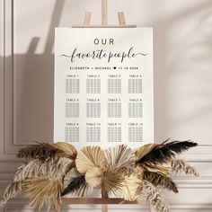 a wedding seating chart is displayed on a wooden easel with feathers and leaves around it