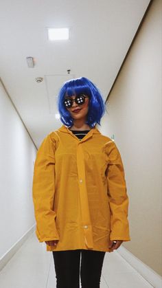 a woman with blue hair wearing a yellow raincoat and black pants in a hallway