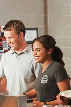 a man and woman standing at a counter preparing food