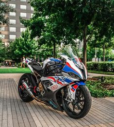 a motorcycle parked on the side of a brick road near trees and bushes in front of a building