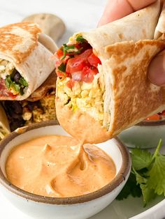 a hand holding a burrito over a bowl of salsa