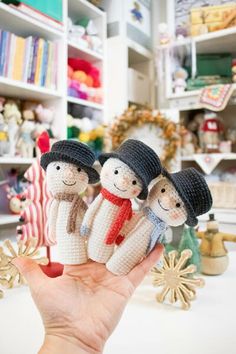 a hand holding three amigurt dolls in front of shelves with other items on it