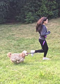 a woman is running with her dog on a leash in the grass near some bushes