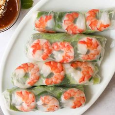 shrimp spring rolls on a white plate with dipping sauce and green leaves next to it