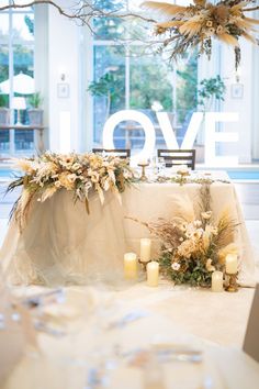 a table with candles and flowers on it in front of a large window that says love