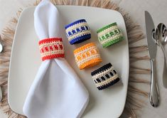 four napkin rings sitting on top of a white plate next to forks and spoons