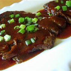 two pieces of meat covered in gravy and green onions on a white plate