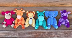 five stuffed animals are lined up in a row on a wooden surface, one is brightly colored and the other is multicolored