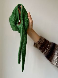 a person's hand holding up a green knitted scarf in front of a white wall