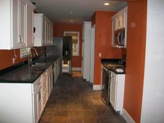 an empty kitchen with white cabinets and black counter tops, along with orange walls in the background