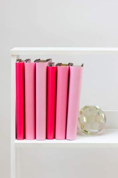 three pink books on a white shelf with a crystal ball in the foreground and another bookcase behind it