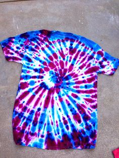 a red, white and blue tie - dye shirt laying on the ground next to a pair of scissors