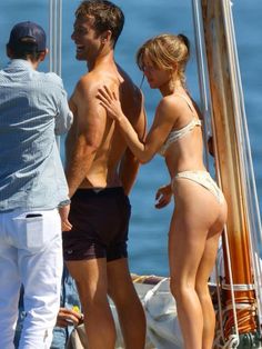 a man and woman standing on the deck of a sailboat talking to each other