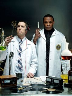 two men in lab coats are holding beaks and looking at the same person with headphones on