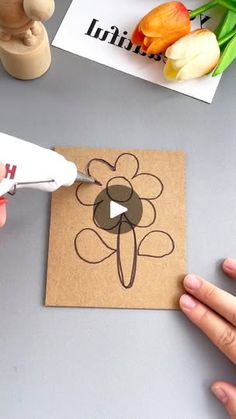 someone cutting out a flower with scissors on top of a piece of brown paper next to tulips