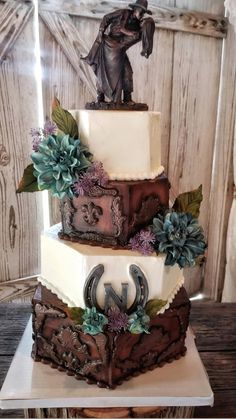 a three tiered cake decorated with flowers and a cowboy figure on top is sitting on a wooden table