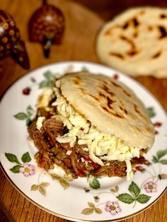 a pulled pork sandwich on a plate with some tortilla bread in the background