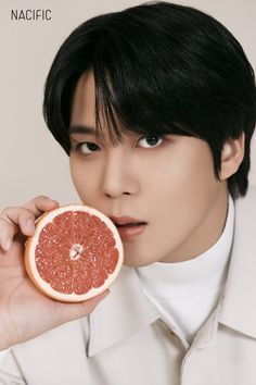 a man is holding a grapefruit in front of his face