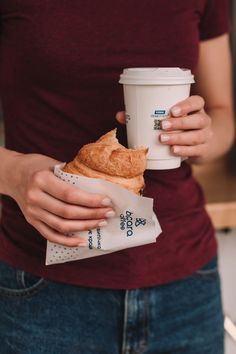 a woman holding a coffee cup and some food in her left hand while wearing a red shirt