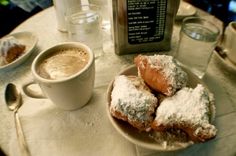 powdered sugar covered doughnuts on a plate next to a cup of coffee