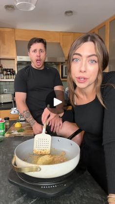 two people in a kitchen cooking food on the stove top and one person standing behind them