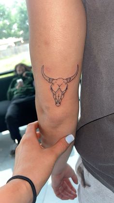 a woman's arm with a tattoo of a bull skull on it and another hand