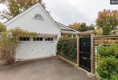 a white house with a black gate in front of it and trees around the driveway