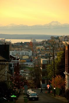 a city street with cars parked on the side and snow capped mountains in the distance