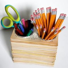 there are many pencils and scissors in the cup on top of a stack of books