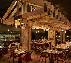 an empty restaurant with wooden tables and chairs in the foreground is lit by hanging lights