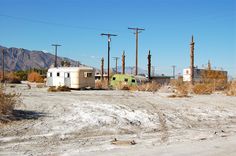 an old trailer sits in the middle of a dirt lot with power lines and telephone poles