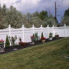 a white picket fence with potted plants in the foreground and flowers on the other side