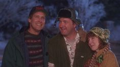 two men and a woman standing next to each other in front of snow covered trees