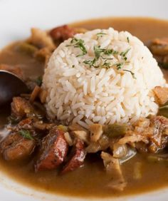 a white plate topped with rice and meat covered in gravy next to a spoon