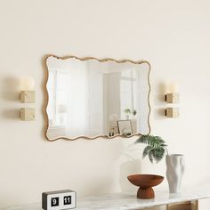 a mirror on the wall above a table with two vases and an alarm clock