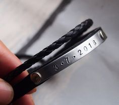 a person is holding a leather bracelet with the date 2013 on it and has two braided ends