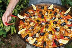 a person holding a pan filled with seafood and rice