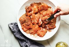 someone is cutting meat into small pieces in a white bowl on a marble counter top