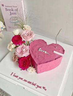 a pink heart shaped cake with flowers and a book