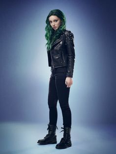 a woman with green hair and black leather jacket standing in front of a blue background