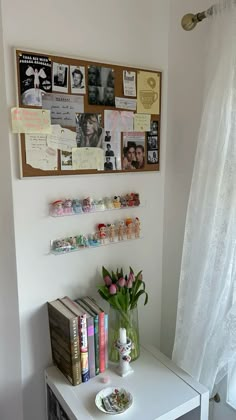 a white table topped with lots of books and vases next to a wall covered in pictures